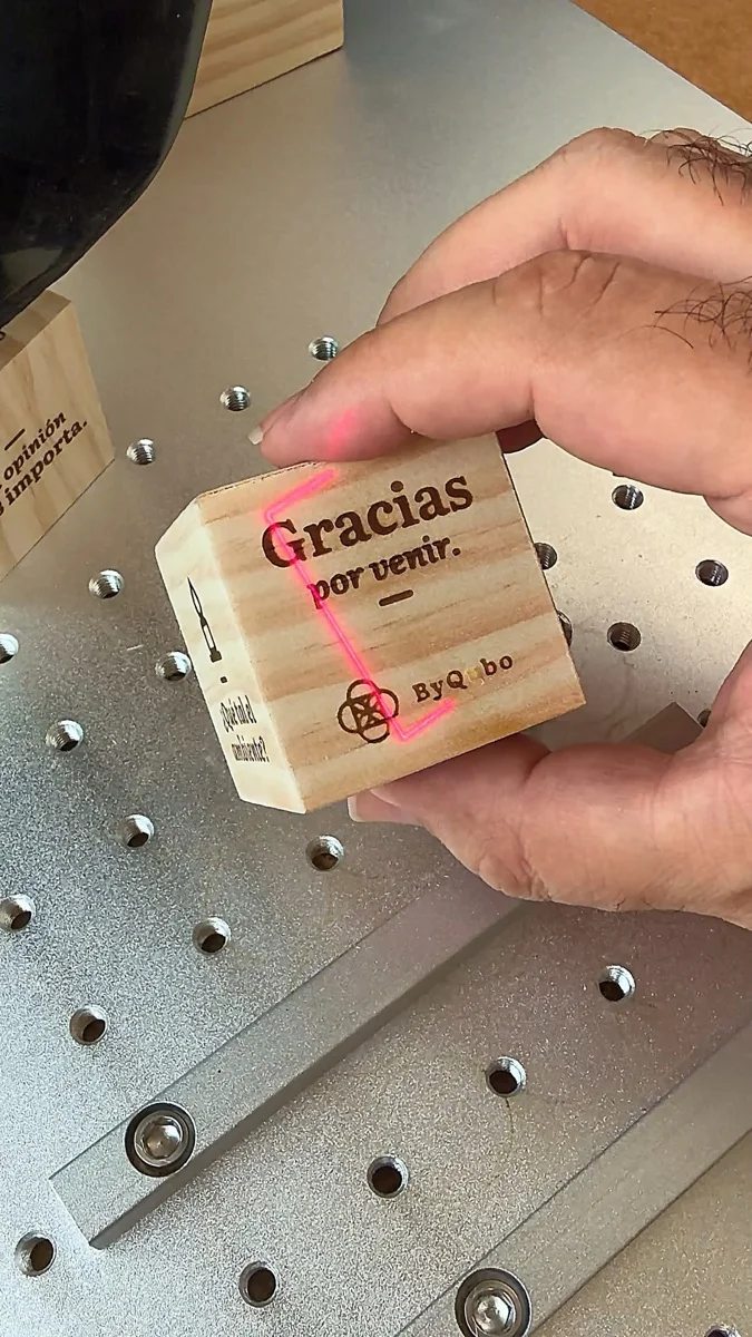 El láser grabando un cubo de pino con el mensaje «Gracias por venir» en el taller