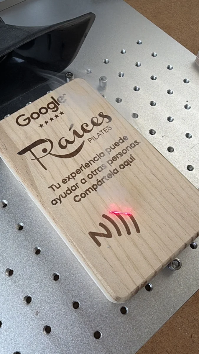 El láser grabando una placa de madera con el logotipo de Raíces Pilates y el símbolo NFC